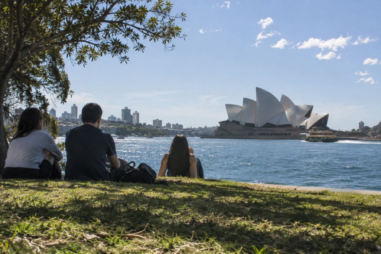 Sydney Opera House sails seen across the water from a harbour foreshore park at midday