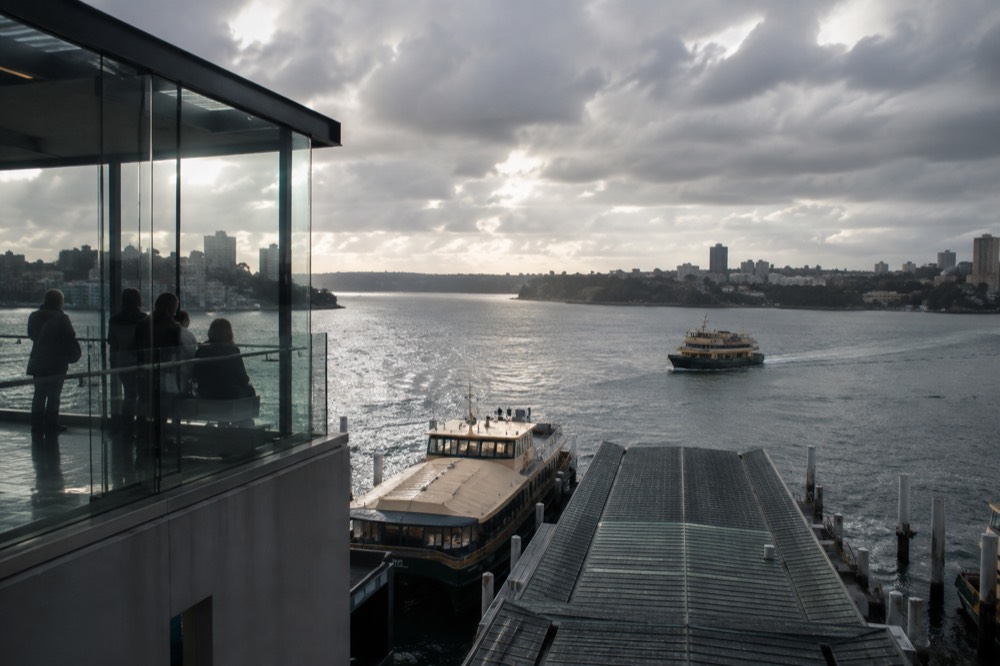 A glass observation deck above the city with rain clouds over the harbour