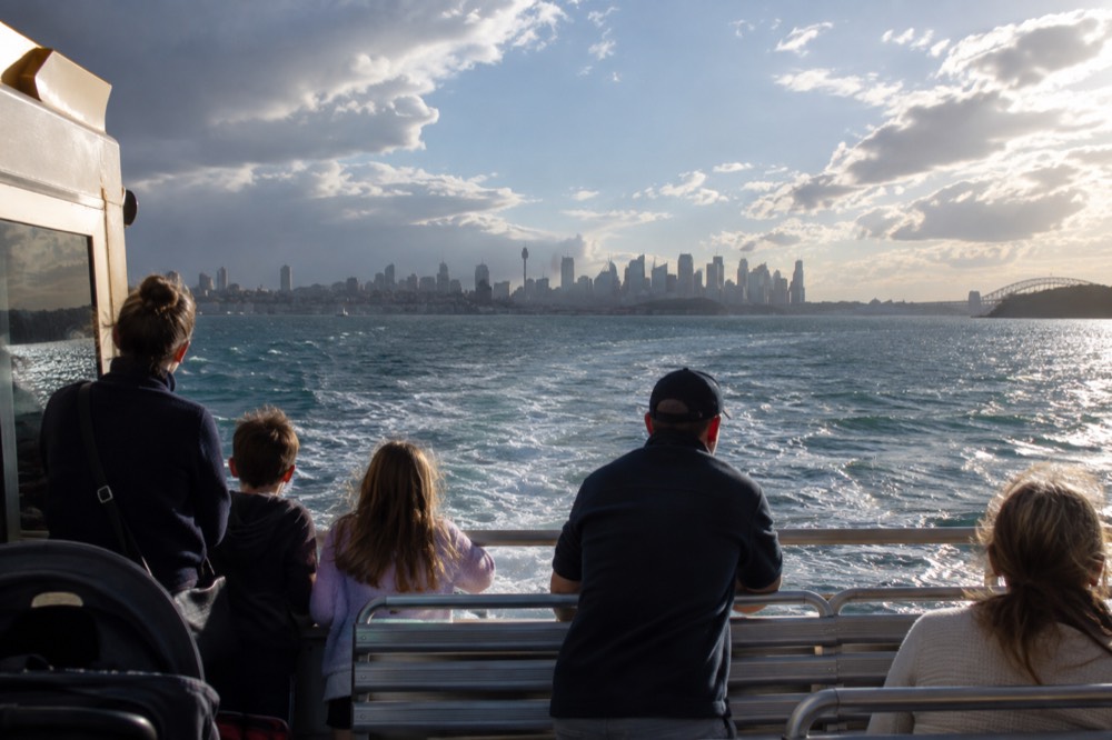 Families on the Manly ferry deck with the city skyline receding across the water